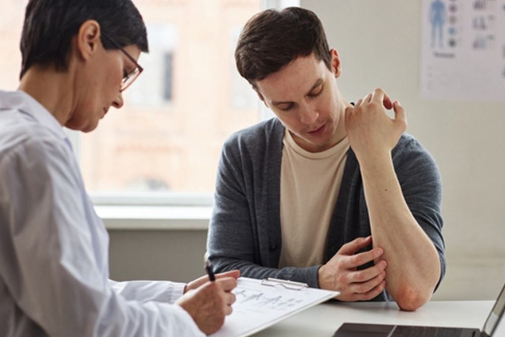 Portrait of young man showing skin rash to doctor during consultation in dermatology clinic